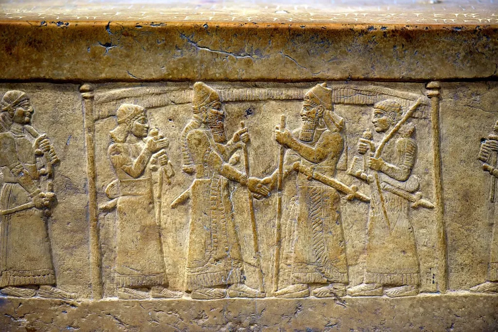An ancient Assyrian stone carving showing two kings clasping hands beneath a canopy, flanked by guards.